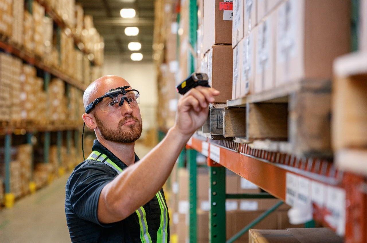 Rugged wearables in action: a male warehouse employee uses a ring scanner and smart glasses to pick stock.