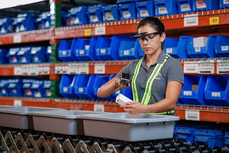 A female worker scans a product using rugged wearables: a ring scanner and smart glasses.