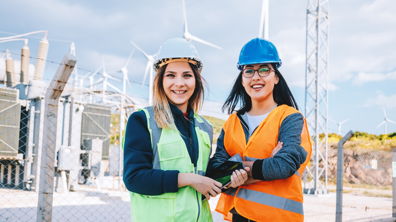 2 female engineers standing in front of a wind farm