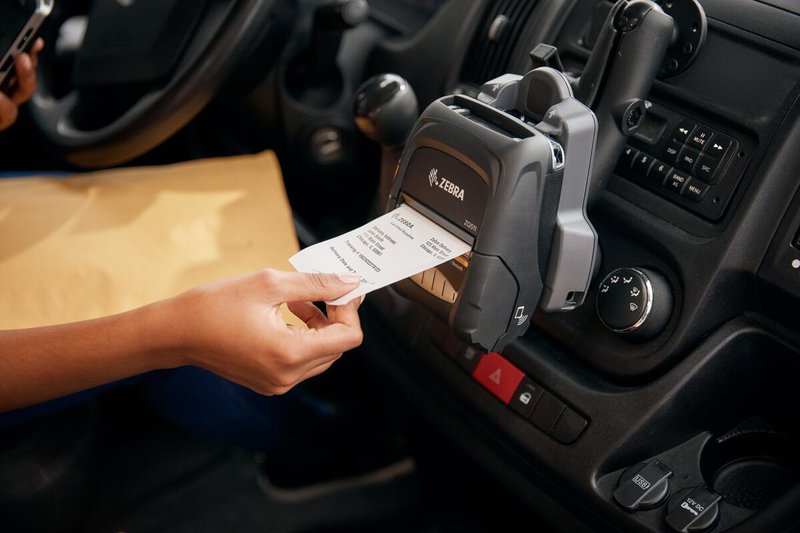 A Zebra Technologies ZQ500 series mobile printer docked in a vehicle, printing a receipt. 