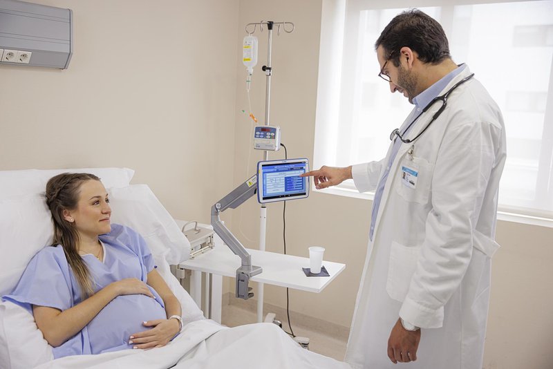 A doctor using a Zebra Technologies ET40 HC to view patient details. The patient is pregnant and lying in a hospital bed.