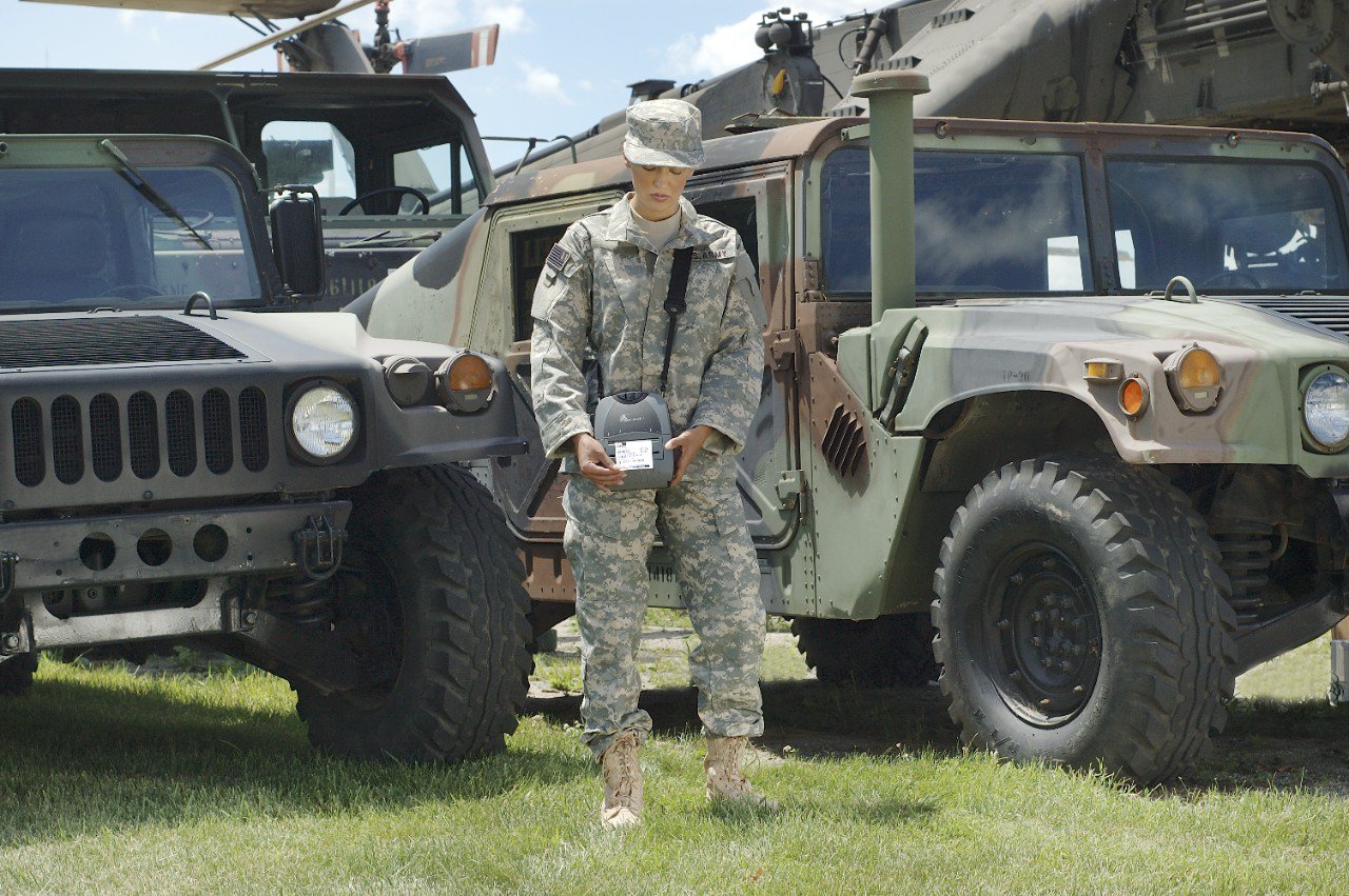 Soldier standing between 2 vehicles looking down at a Zebra Technologies mobile label printer