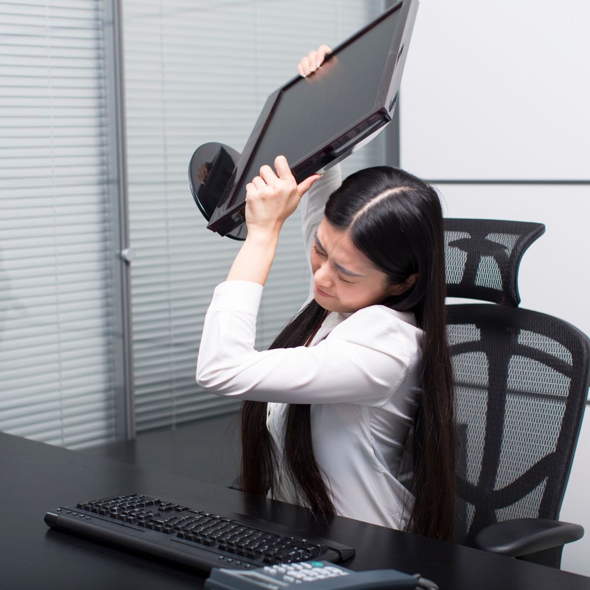 Office worker sitting at her desk throwing a computer monitor because she is frustrated by untested updates affecting her computer.